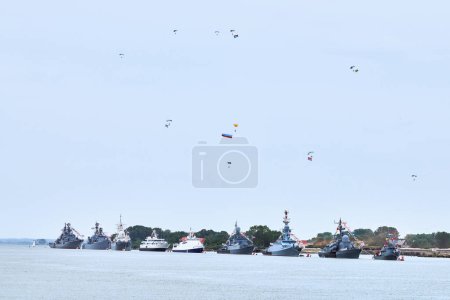 Photo for Airborne forces paratroopers flying Russian flag over naval forces parade warships along coastline, seafaring tradition of military ships formation at Navy Day, nautical spectacle of russian sea power - Royalty Free Image