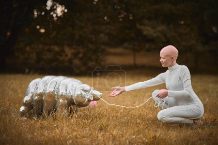 Retrato de una joven sin pelo con alopecia en tela blanca jugando con un juguete tardígrado en el parque de otoño, escena surrealista con una adolescente calva reflexionar sobre los hilos entrelazados de la vida y el arte