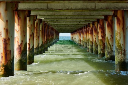 Rusty pillars of old sea pier create mesmerizing seascape scene with view from under pier, restless sea waves crashing on rock symbolizing harmonious yet powerful coastal symphony