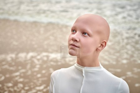 Photo for Close up portrait of young hairless girl with alopecia in white futuristic costume on sea background, bald pretty teenage girl showcasing unique beauty and identity with pride, unusual alien girl - Royalty Free Image