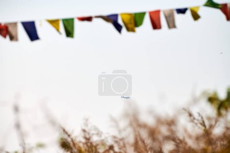 Des drapeaux de prière tibétains colorés flottent d'anciennes prières dans un vent de montagne serein au sommet d'une haute colline sur fond de ciel bleu avec des avions touristiques qui volent au loin vers la montagne de l'Everest