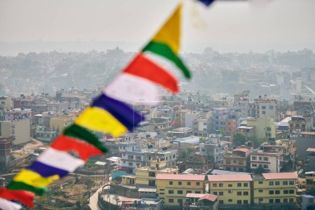 View of Kathmandu with lot of low rise buildings through colorful prayer flags, hilltop view of Kathmandu cityscape creating harmonious blend of spirituality and urbanity