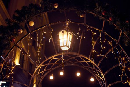 Weihnachtsbeleuchtung, die den Torbogen in der Silvesternacht schmückt, verleiht der nächtlichen Szenerie ein gemütliches Ambiente, gelbes geheimnisvolles Licht, das festliches Staunen und Freude hervorruft, magische Neujahrsatmosphäre