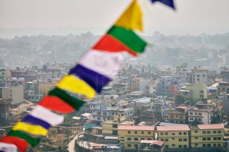 Blick auf Kathmandu mit vielen Flachbauten durch bunte Gebetsfahnen, Blick auf das Stadtbild von Kathmandu auf den Hügeln, die eine harmonische Mischung aus Spiritualität und Urbanität schaffen