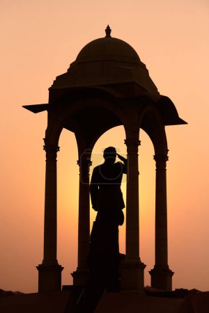 Silueta de Subhas Chandra Bose estatua bajo dosel detrás de la puerta de la India monumento de guerra en glorioso atardecer, monolítico Netaji estatua hecha de granito negro en Nueva Delhi inmortaliza indio luchador por la libertad