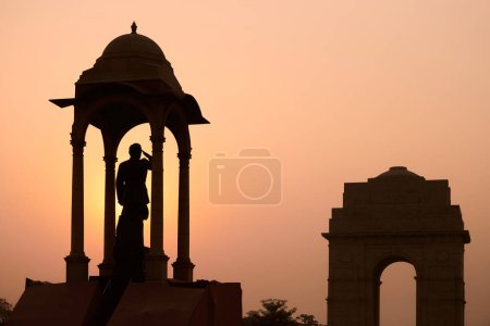 Silhouette of Subhas Chandra Bose statue under canopy behind India Gate war memorial in glorious sunset, monolithic Netaji statue made of black granite in New Delhi immortalizes Indian freedom fighter
