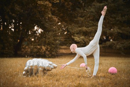 Photo for Portrait of young hairless girl ballerina with alopecia in white cloth playing with tardigrade toy in fall park, surreal scene with bald teenage girl reflect on intertwining threads of life and art - Royalty Free Image