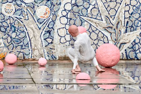 Baile al aire libre de la joven bailarina con alopecia en traje futurista blanco con movimientos plásticos y flexibles entre esferas rosadas sobre fondo abstracto mosaico soviético, simboliza la autoexpresión