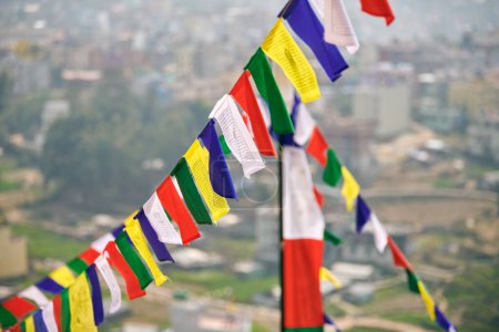 Drapeaux de prière tibétains colorés sur fond flou de paysage urbain de Katmandou symbolisant la valeur culturelle et le patrimoine spirituel de la région népalaise, connexion entre les royaumes terrestres et spirituels
