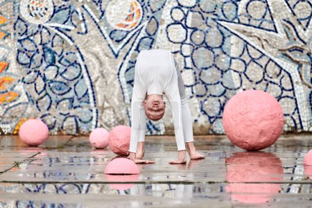 Baile al aire libre de la joven bailarina con alopecia en traje futurista blanco con movimientos plásticos y flexibles entre esferas rosadas sobre fondo abstracto mosaico soviético, simboliza la autoexpresión