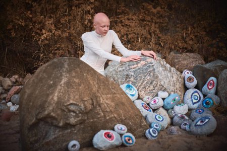 Jeune fille sans cheveux avec alopécie en costume futuriste blanc regardant le paysage surréaliste avec beaucoup d'yeux de rochers, symbolisant la connexion entre l'esprit humain et la terre