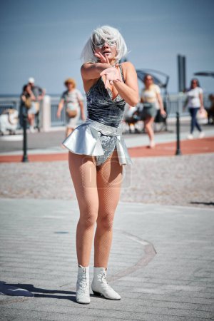 Junge sexy Mädchen im silbernen Mikrorock tanzen mit sanften, femininen und anmutigen Bewegungen, weibliche Outdoor-Tanzdarbietungen auf der Strandpromenade schaffen ein aufregendes Outdoor-Spektakel
