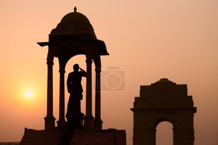Silueta de Subhas Chandra Bose estatua bajo dosel detrás de la puerta de la India monumento de guerra en glorioso atardecer, monolítico Netaji estatua hecha de granito negro en Nueva Delhi inmortaliza indio luchador por la libertad