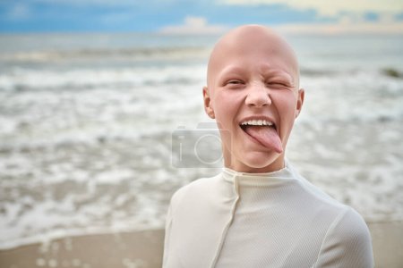 Hairless girl with alopecia make faces in white futuristic costume on sea background, close up portrait of bald pretty teenage girl showcasing unique beauty and identity with pride, unusual alien girl