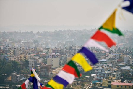 View of Kathmandu with lot of low rise buildings through colorful prayer flags, hilltop view of Kathmandu cityscape creating harmonious blend of spirituality and urbanity