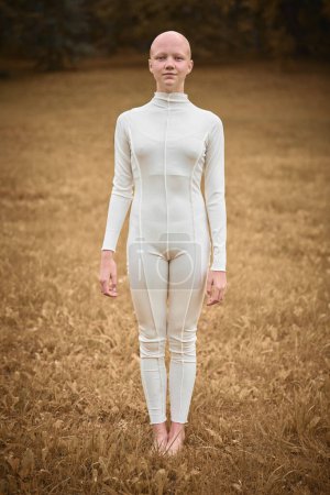 Full length portrait of young hairless girl with alopecia in white cloth on autumn park background, bald pretty teenage girl symbolizing acceptance of her unique beauty individuality and beauty