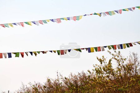 Bunte tibetische Gebetsfahnen flattern uralte Gebete in den ruhigen Gebirgswind auf einem hohen Hügel vor blauem Himmel und symbolisieren spirituelle Energie und friedliche Ruhe.