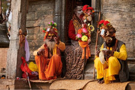 Téléchargez les photos : Katmandou, Népal - 01.02.2023 - Trois Sadhu vêtus de vêtements de couleur safran se trouve dans l'ancien sanctuaire votif de Pandra Shivalaya dans le temple de Pashupatinath, ascète Sadhu priant et mendiant pour l'aumône - en image libre de droit