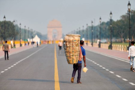 Foto de Nueva Delhi, India - 23.10.2022 - Vendedor ambulante indio de puri que lleva una cesta grande a sus espaldas con pan frito poori, caminatas callejeras huckster en el bulevar Rajpath en Nueva Delhi - Imagen libre de derechos