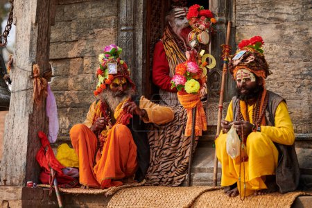 Téléchargez les photos : Katmandou, Népal - 01.02.2023 - Trois Sadhu vêtus de vêtements de couleur safran se trouve dans l'ancien sanctuaire votif de Pandra Shivalaya dans le temple de Pashupatinath, ascète Sadhu priant et mendiant pour l'aumône - en image libre de droit