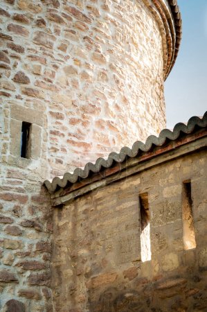 Nahaufnahme eines alten Steinturms mit kleinen Fenstern, der eine strukturierte Oberfläche und traditionelles architektonisches Design präsentiert. Beleuchtet durch natürliches Licht.