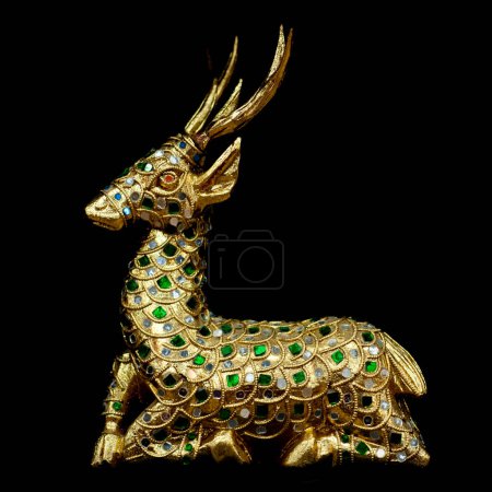 A detailed golden deer statue adorned with green and blue gemstones, captured against a black background. The craftsmanship highlights intricate designs and patterns