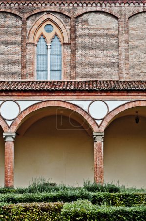 Foto de Un patio sereno dentro de la Basílica de San Francesco en Bolonia, Italia. Columnas de ladrillo rojo, enmarcar el espacio abierto. Exuberante vegetación y sencillez definen esta iglesia franciscana principal - Imagen libre de derechos