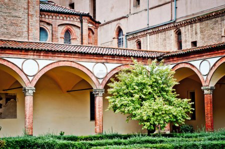 Foto de Un patio sereno dentro de la Basílica de San Francesco en Bolonia, Italia. Columnas de ladrillo rojo, enmarcar el espacio abierto. Exuberante vegetación y sencillez definen esta iglesia franciscana principal - Imagen libre de derechos