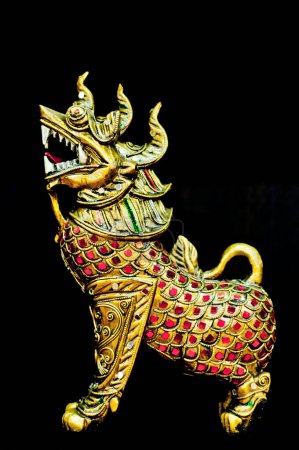 Foto de Una estatua de oro detallada de una criatura mítica, posiblemente un dragón o un león, adornada con intrincados diseños y adornos de piedras preciosas rojas. La figura es capturada sobre un fondo oscuro, destacando sus rasgos ornamentados. - Imagen libre de derechos