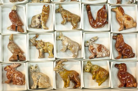 A variety of glazed ceramic animal figurines neatly arranged in white boxes, showcasing different species including birds, cats, and rabbits.
