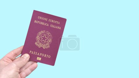 Foto de Pasaporte biométrico italiano de la Unión Europea sostenido a mano aislado sobre un fondo azul claro - Imagen libre de derechos