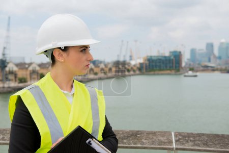 Retrato de una mujer joven que trabaja en la industria de la construcción de edificios, con casco de seguridad blanco y chaleco amarillo de alta visibilidad.