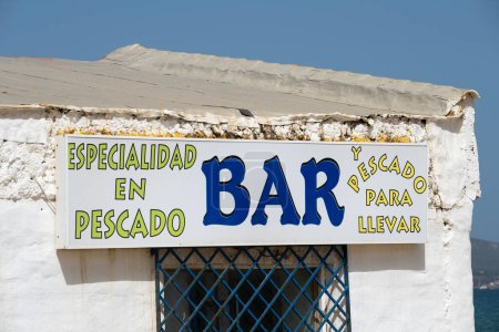 Cartel en el exterior de un bar rústico pintado de blanco, especializado en comida de mar con servicio de comida para llevar, en la playa de Algeciras en España.