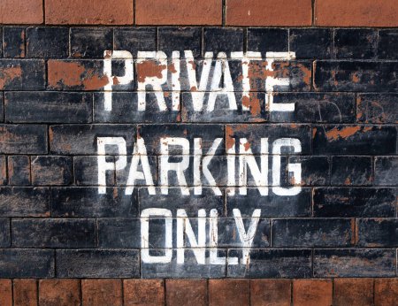 PRIVATE PARKING ONLY hand painted weathered sign with white lettering and black background, onto building exterior with red brick. 