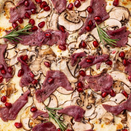 Foto de Primer plano de relleno y textura de pizza, carne roja, granada, lavabos y romero en la parte superior - Imagen libre de derechos