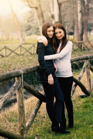 Foto de Intenso retrato de cuerpo completo de hermanas jóvenes abrazándose al aire libre en un parque. - Imagen libre de derechos