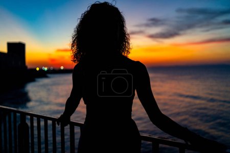 Téléchargez les photos : Portrait de femme silhouette face à la mer au coucher du soleil. Image de style de vie réel. - en image libre de droit