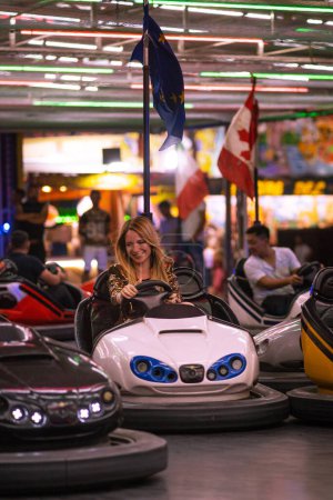 Téléchargez les photos : Jeune portrait de femme blonde souriante s'amusant sur Luna Park la nuit avec des voitures pare-chocs. - en image libre de droit