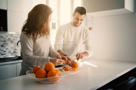 Téléchargez les photos : Jeune couple heureux préparant le petit déjeuner, serrant des oranges, à la maison le matin. Concept de mode de vie sain avec éruption solaire. Focus sur les mains. - en image libre de droit