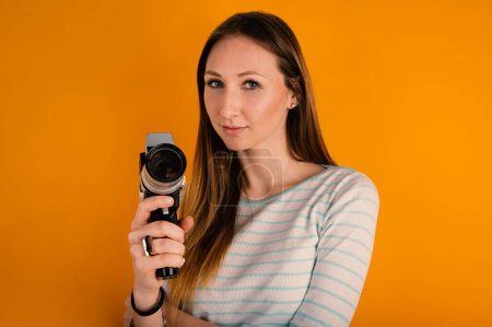 Foto de Mujer sosteniendo la cámara de vídeo de película vintage de cerca contra fondo naranja. Retrato de estudio. - Imagen libre de derechos