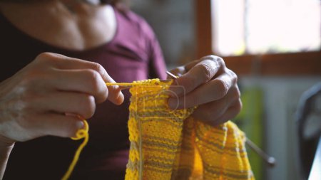 Foto de Mujer de mediana edad tejiendo una bufanda de colores en casa, primer plano de las manos. Estilo de vida. Imagen filtrada. - Imagen libre de derechos