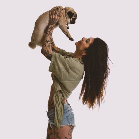Foto de Atractiva mujer tatuada divirtiéndose con su perro. Retrato de estudio. - Imagen libre de derechos