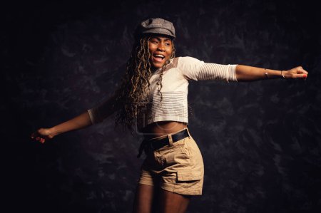 Foto de Hermosa sonriente mujer negra africana bailando estudio retrato sobre fondo oscuro. - Imagen libre de derechos