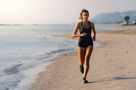 Photo for Young woman full body portrait running outdoors on the beach in the morning. - Royalty Free Image