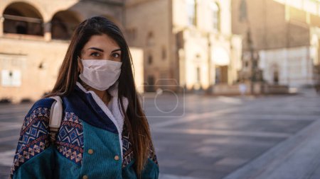 Photo for Young woman wearing face mask for protection in a deserted city due to Covid-19 Corona virus. Bologna, Italy. - Royalty Free Image