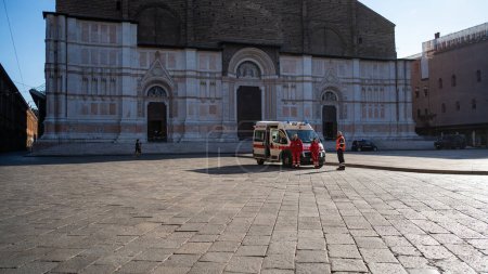 Foto de BOLOGNA, ITALIA - MARZO 2020: Ambulancia y paramédicos frente a la Catedral de San Petronio, Piazza Maggiore, durante la infección pandémica por el virus Covid-19. - Imagen libre de derechos
