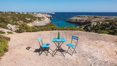 Photo for Table and chairs with bottle in a scenic position facing the Binidali bay. Menorca, Spain. - Royalty Free Image