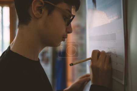 Téléchargez les photos : Adolescent garçon écrit des notes sur le calendrier à la maison. Image filtrée. - en image libre de droit
