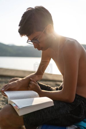 Téléchargez les photos : Jeune garçon relaxant lisant un livre en été. - en image libre de droit