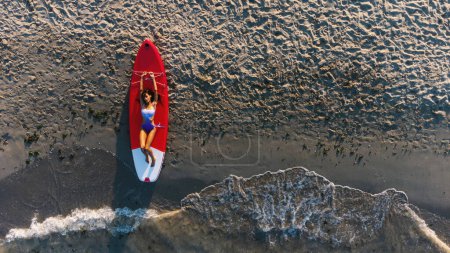 Photo for Young attractive woman portrait on Stand Up Paddle Board, SUP, in a sunny day on the beach. Aerial top down view. - Royalty Free Image